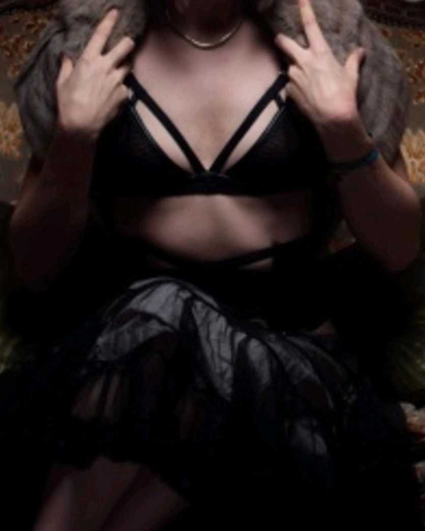 Mastress Caer seated in dark lingerie and a fur wrap, face out of frame.